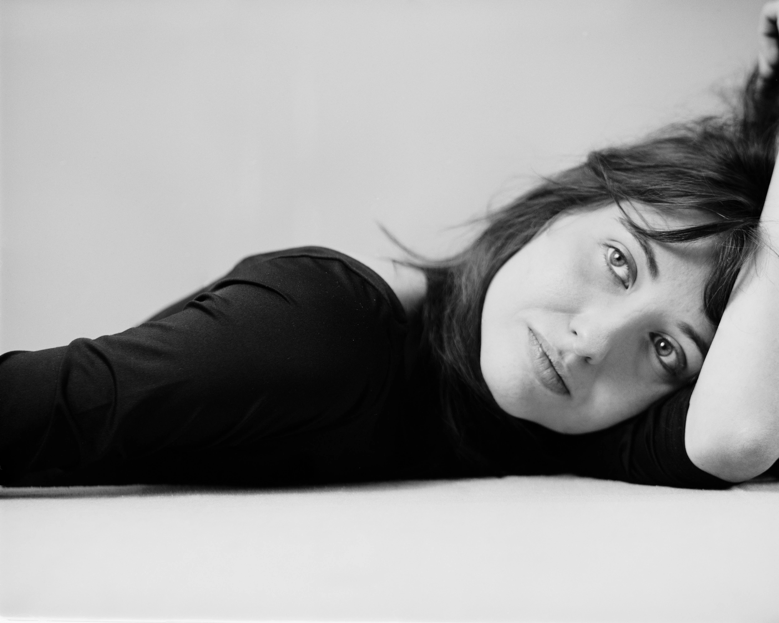 Black and white portrait of a young woman resting her head against her arm.
